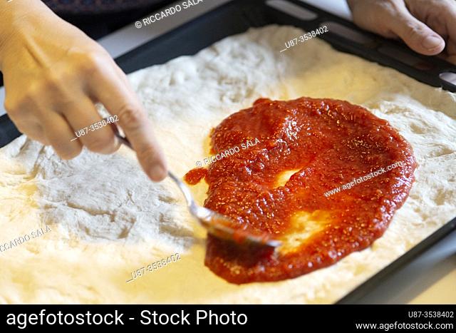 Woman Spreading Tomato Sauce on Homemade Rustic pizza. .