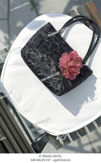 Handtasche aus glaenzendem Stoff auf einem Gartenstuhl - Accessoire - Textilien , Handbag made of shiny Cloth on a Lawn Chair - Accessory - Textiles