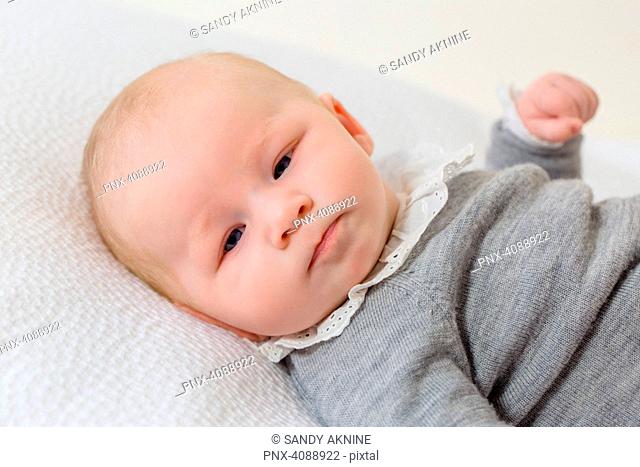 Close-up of a young infant in grey layette of 2 months elongate on a whitebed