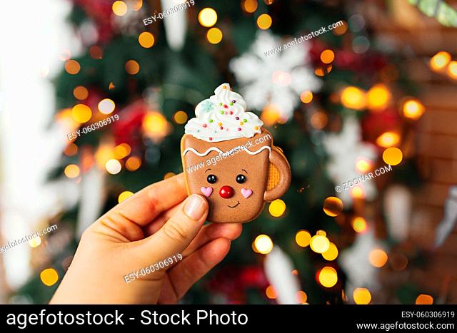 Hand holding christmas gingerbread cookie and decorations at christmas tree, gingerbread cup. High quality photo