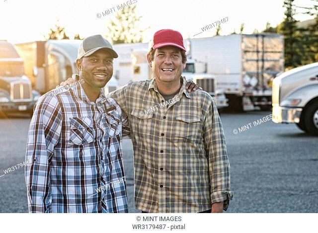 A Caucasian man and a black man truck driving team together in a truck stop parking lot