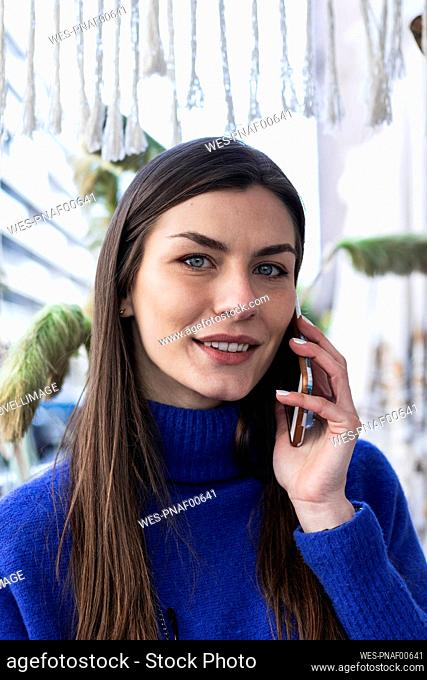 Smiling woman with gray eyes talking on mobile phone against plant