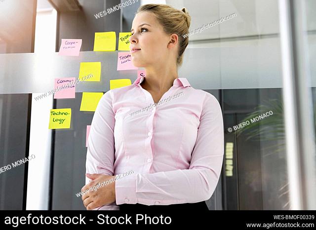 Young businesswoman, standing in front of adhesive notes, with arms crossed