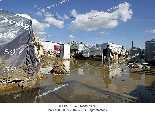 30 January 2019, Lebanon, Al Marj: A Syrian refugee wades through an area flooded by rain water amongst the tents of Al Marj refugee camp