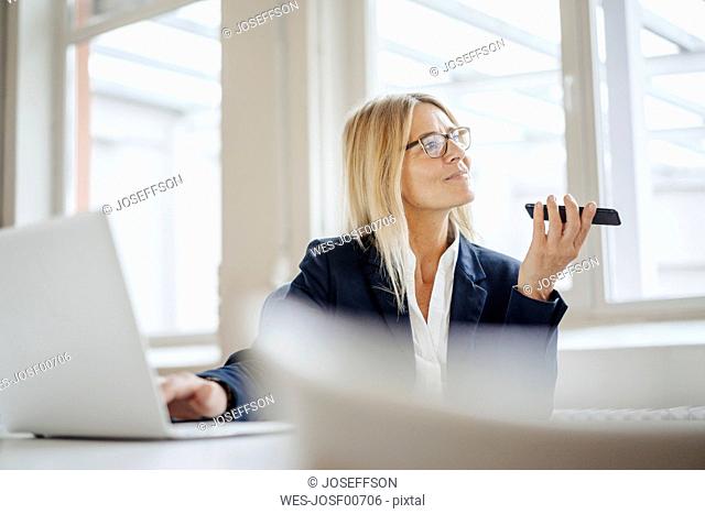 Businesswoman using laptop and cell phone in office