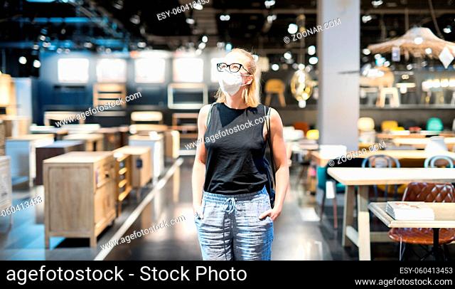 New normal during covid epidemic. Caucasian woman shopping at retail furniture and home accessories store wearing protective medical face mask to prevent...