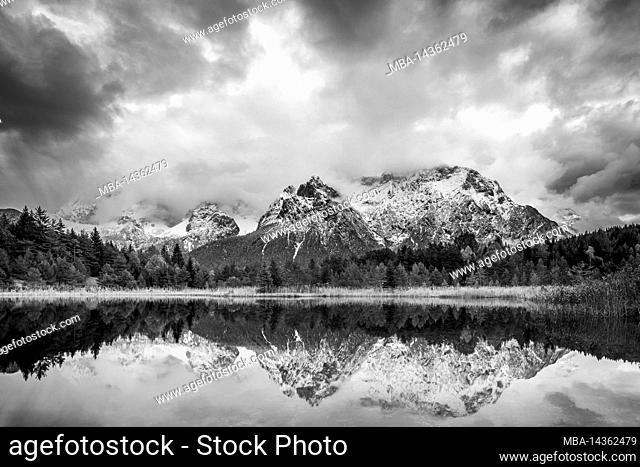 The Karwendel mountains are reflected in the Luttensee lake near Mittenwald. Fresh snow and atmospheric clouds frame the mountains