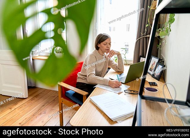 Freelancer writing on documents with pen at desk