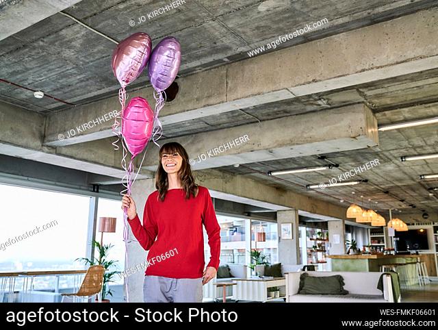 Businesswoman holding balloons while standing in loft office