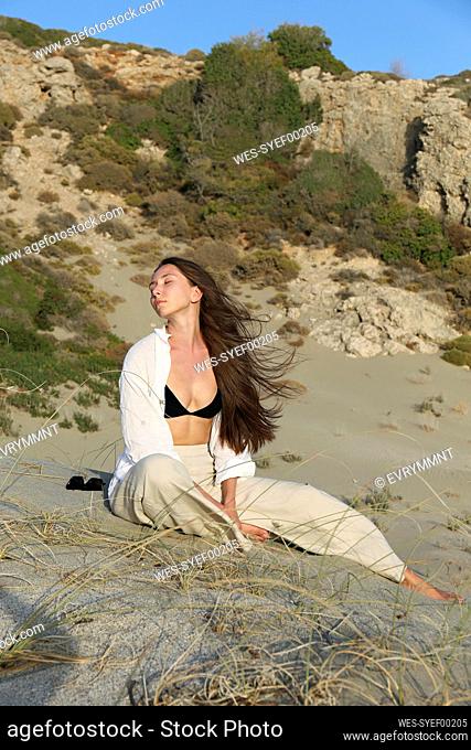 Young woman with eyes closed sitting on sand at beach, Patara, Turkiye