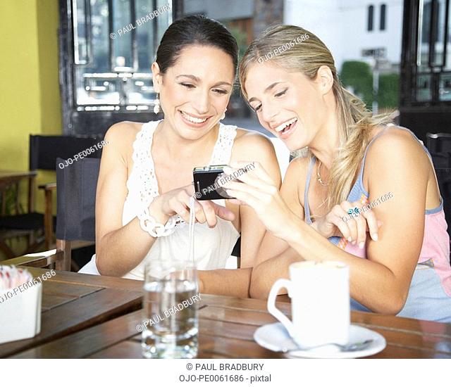 Two women in restaurant looking at digital camera pointing and smiling