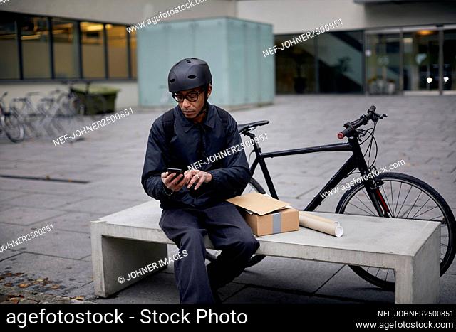 Bicycle courier using cell phone on bench