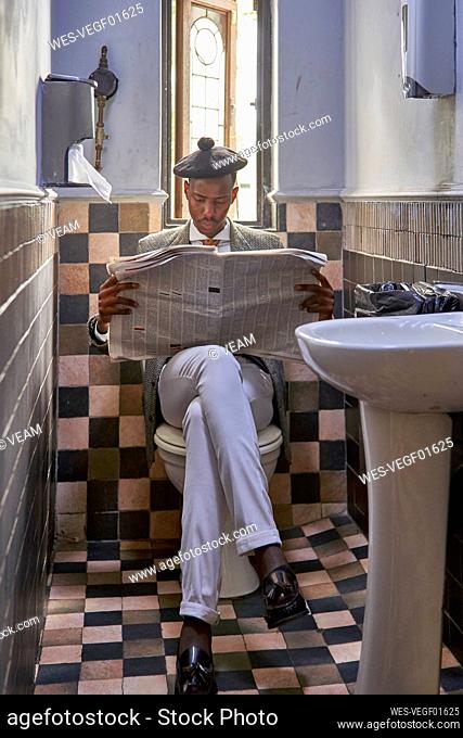 Stylish young businessman with a beret reading the newspaper sitting in the restroom
