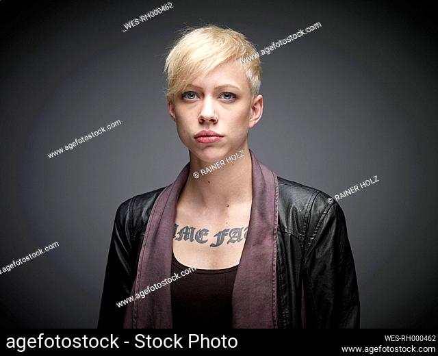 Portrait of blond young woman with tatoo in front of grey background