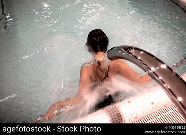 Woman Relaxing in a Hydro Massage Pool with Falling Water on Her Spine and Neck in Switzerland