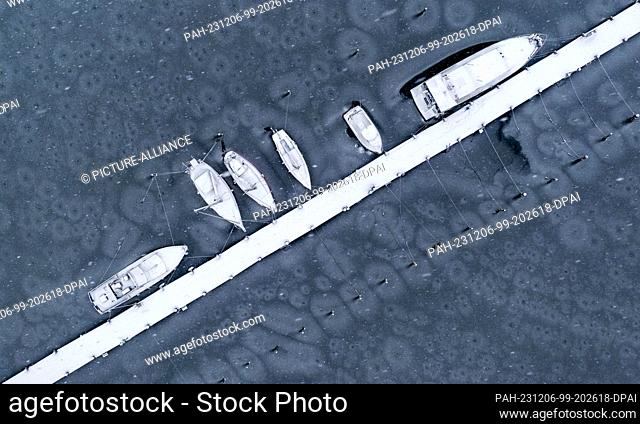 06 December 2023, Mecklenburg-Western Pomerania, Kirchdorf (poel): Boats covered in snow lie frozen in thin ice on a jetty in the harbor on the Baltic Sea...