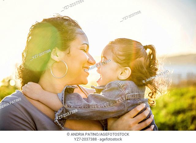 Mother and daughter embracing with the sun behind them