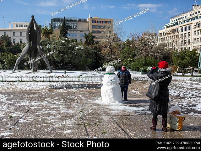 17 February 2021, Greece, Athen: A woman takes a photo of a man standing next to a snowman in central Athens. A strict lockdown has been in effect for the...