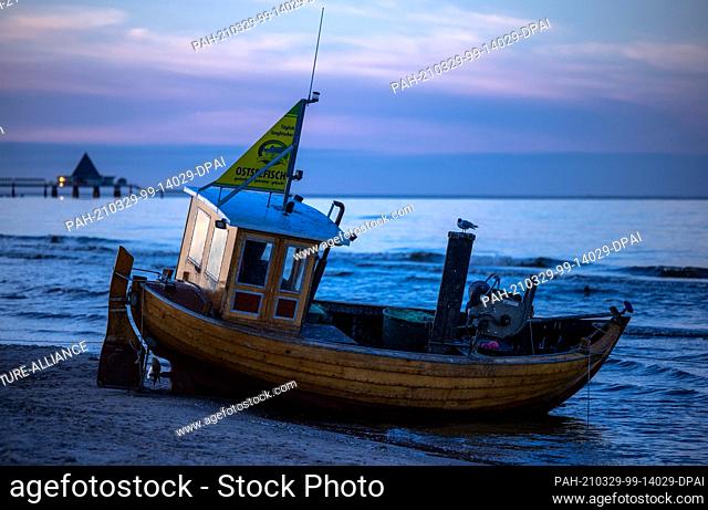 22 March 2021, Mecklenburg-Western Pomerania, Ahlbeck: A wooden fishing boat lies on the beach in front of the pier of Heringsdorf