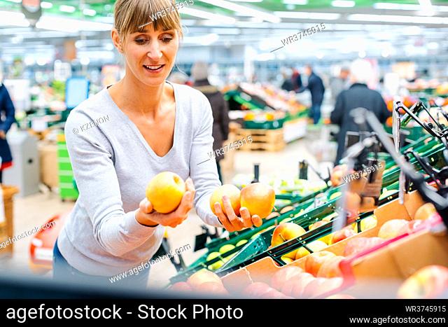 Woman testing the fresh fruit in a supermarket shelf holding apples in her hand