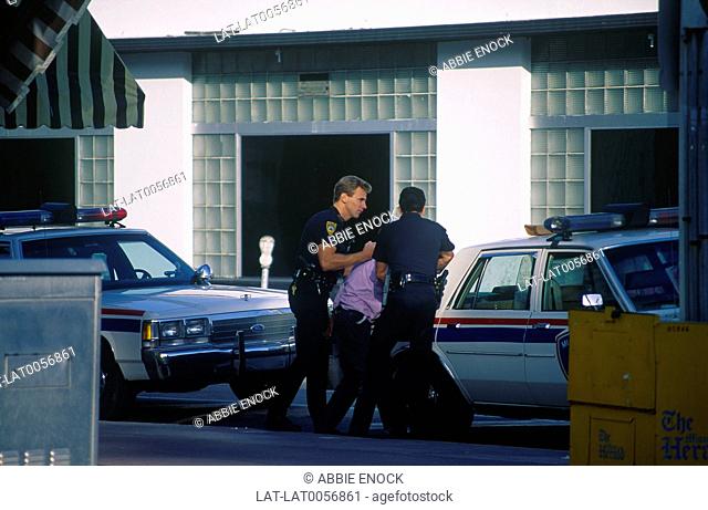 South Miami Beach. Ocean Drive.Two policemen arresting man in lilac shirt. Police cars