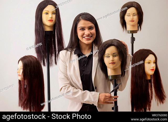 A YOUNG HAIR STYLIST HAPPILY POSING WITH DUMMY HAIR