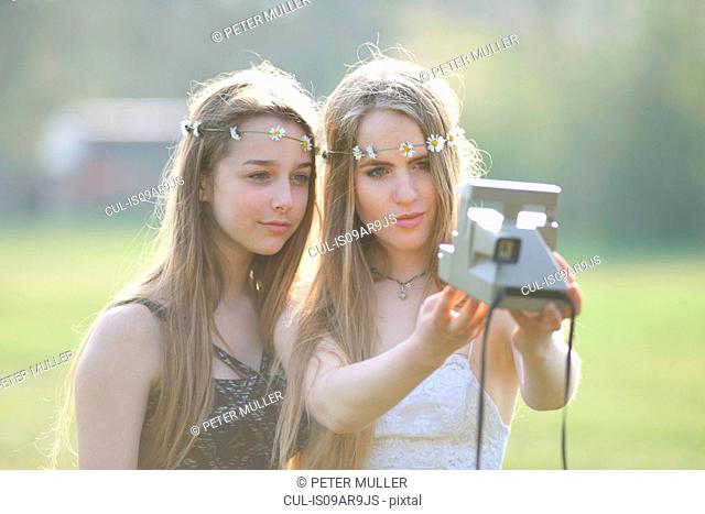 Two teenage girls in park taking instant camera selfie