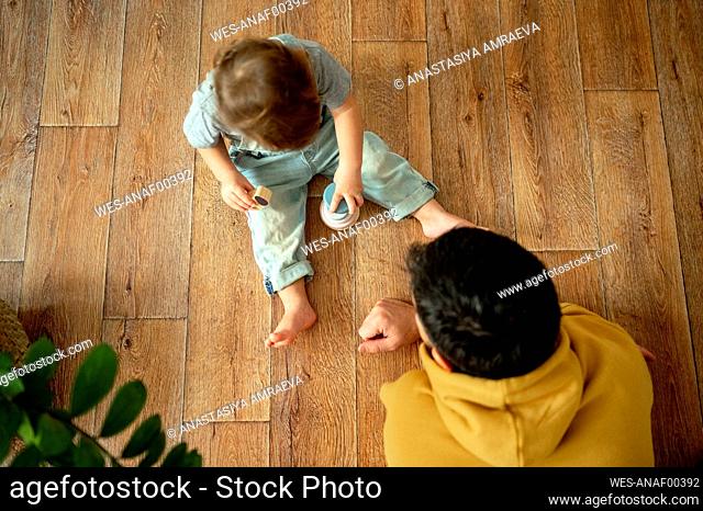 Father playing with boy on hardwood floor at home