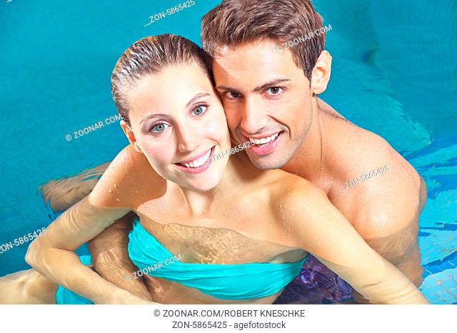 Zufriedenes Paar sitzt lächelnd zusammen im Wasser vom Pool eines Hotels