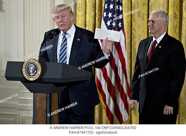 United States President Donald Trump holds up an envelope that was left for him in the Oval Office by former US President Barack Obama next to US Vice President...
