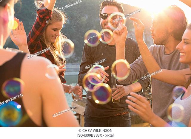 Adult friends playing with floating bubbles at roof terrace party