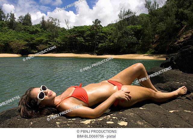 Pacific Islander woman sunbathing on rocks next to water