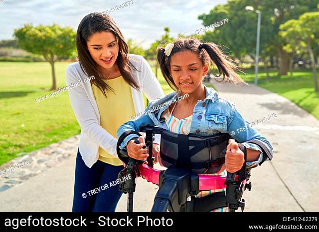Mother helping disabled daughter walking in rollator at park