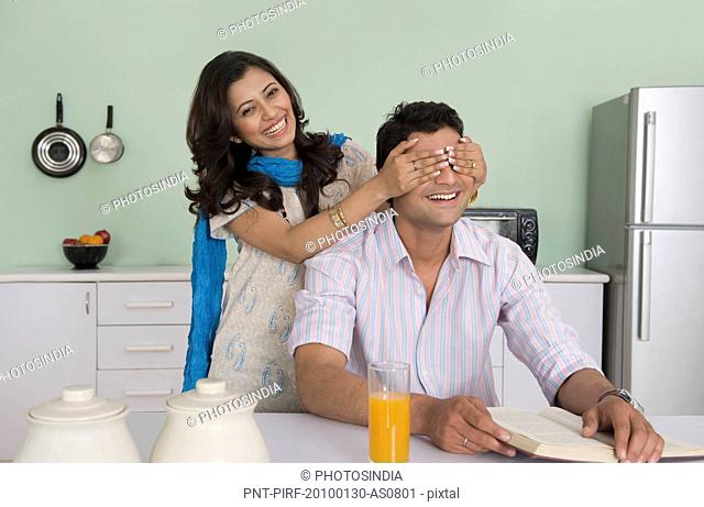 Woman covering her husband's eyes at a dining table