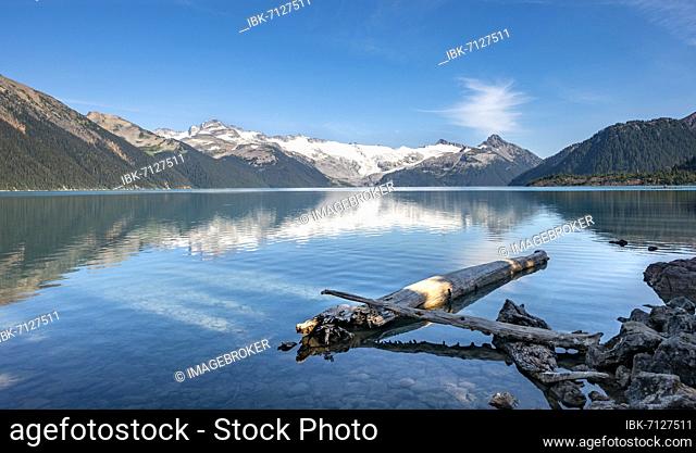 Garibaldi Lake, tree trunks on the shore, mountains reflected in the turquoise glacial lake, Guard Mountain and Deception Peak, glacier in the back