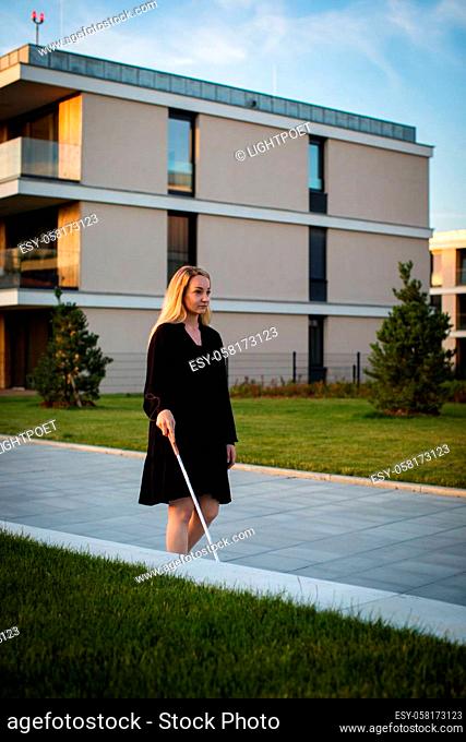 Blind woman walking on city streets, using her white cane to navigate the urban space better and to get to her destination safely