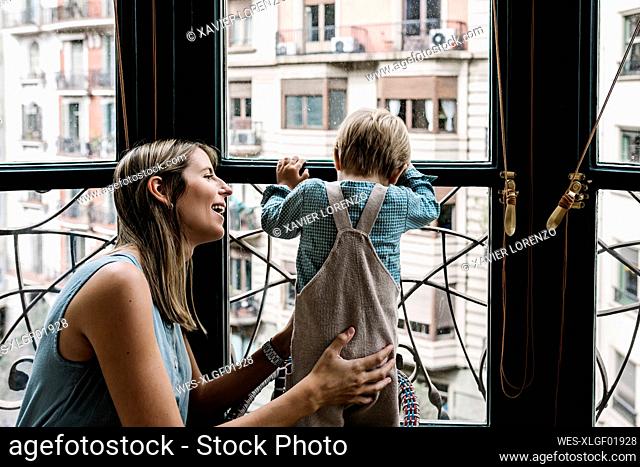 Mother holding son looking through window at home