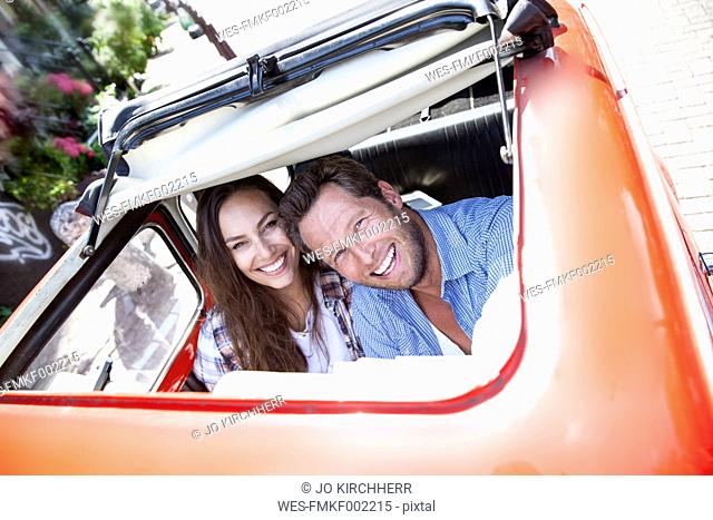 Happy couple looking through open sunroof of a small car