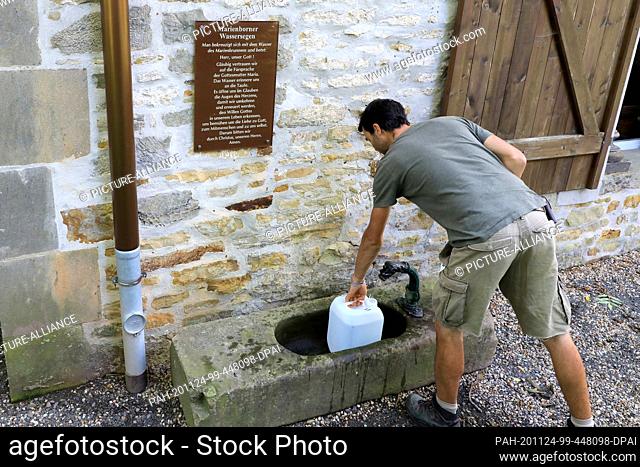 03 October 2020, Saxony-Anhalt, Marienborn: A man fills his canister with water at the water blessing point at the Marienkapelle of the pilgrimage site...