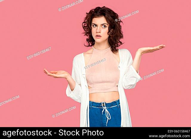 Left or right? Portrait of doubtful beautiful brunette young woman with curly hairstyle in casual style standing, raised arms and confused for choose