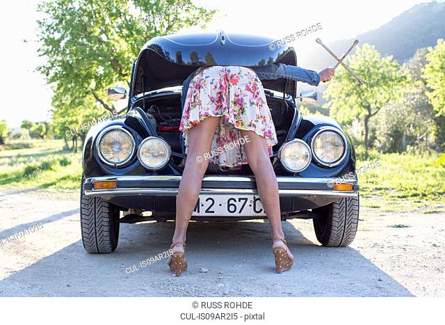 Mature woman bent over car, looking in bonnet