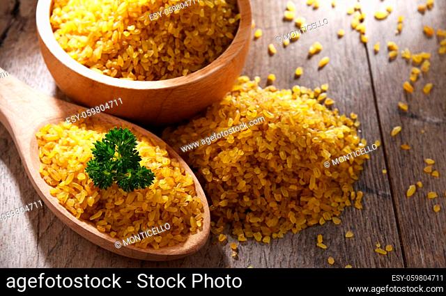 Composition with a bowl and spoon of uncooked bulgur on a table