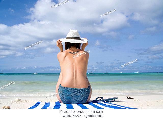 young topless woman with sun hat relaxes on the beach, Philippines