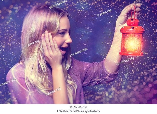 Portrait of a beautiful excited woman surprised looking on a glowing light in lantern, true miracle in Christmas eve, happy magical night