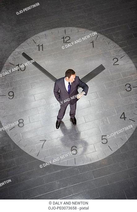 Businessman standing in center of large clock and checking time on wristwatch