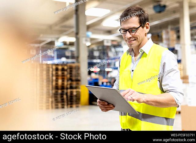 Smiling worker wearing eyeglasses using tablet PC in warehouse