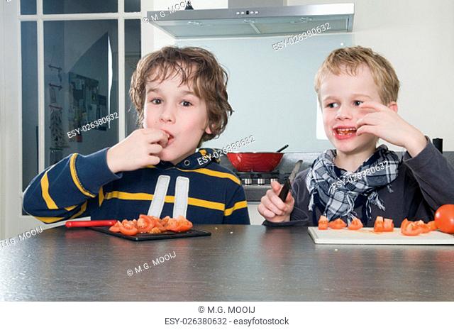 Two boys tasting the just cutted tomatos, used for cooking