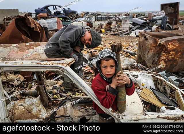 02 March 2021, Syria, Idlib: Malik Junaid (L), 9-years-old, sits on top of a destroyed car next to the 7-years-old Abdel Karim Hassan who carries a mortar shell