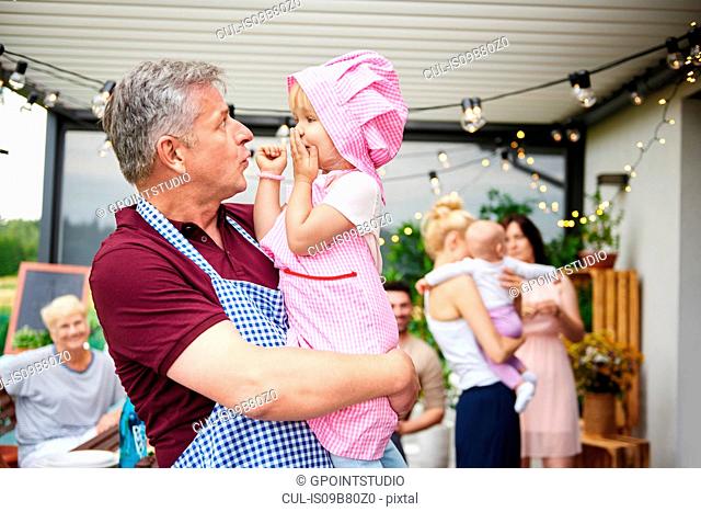 Mature man making faces at toddler granddaughter at family lunch on patio
