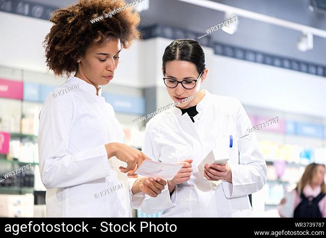Two female pharmacists reading the information from the pack of a new product while comparing two different medicines regarding indications and side effects